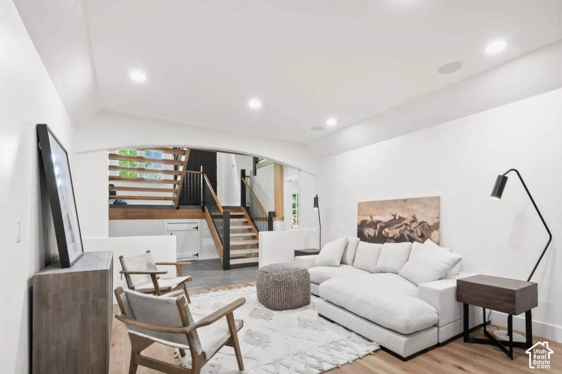 Recessed lighting illuminates the open-concept space featuring wood-finish flooring and a contemporary staircase with wood treads and black railings