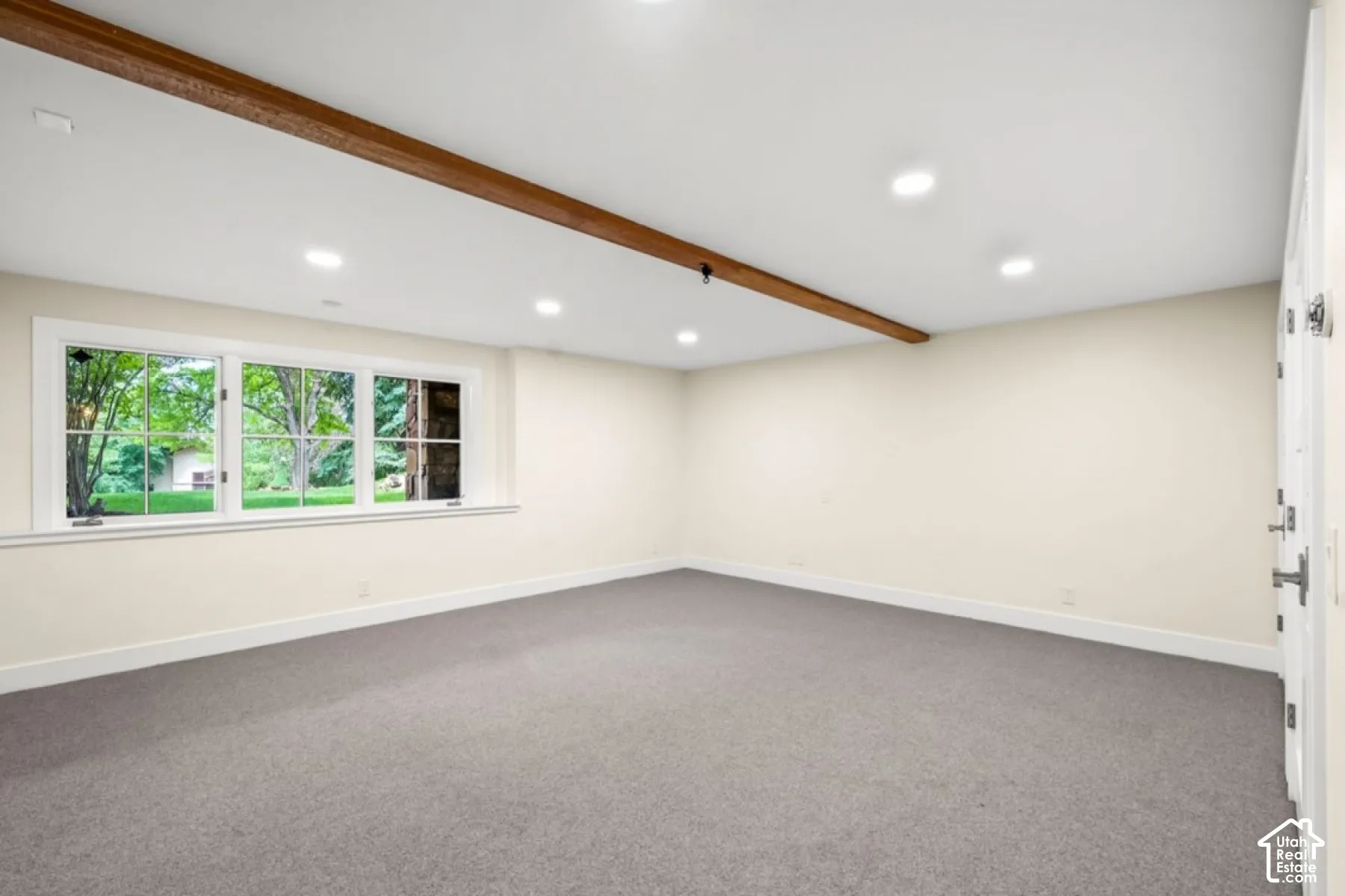 Recessed lighting, wood-beam ceiling accent, wall-to-wall carpeting, white trim, and a multi-pane window