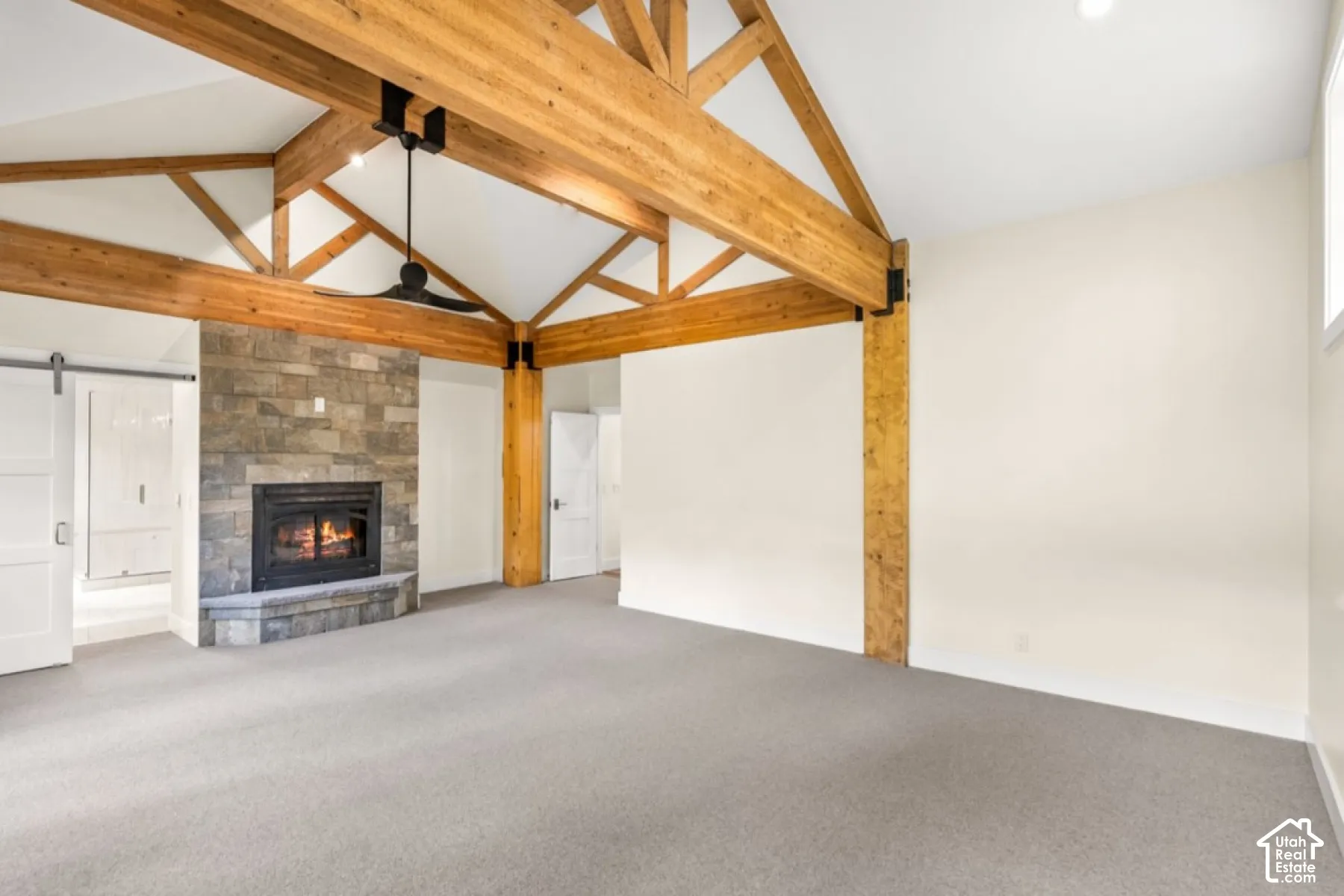 Vaulted ceiling with exposed wood beams, stone-clad fireplace, built-in fireplace insert, neutral carpeting, and a barn door entry