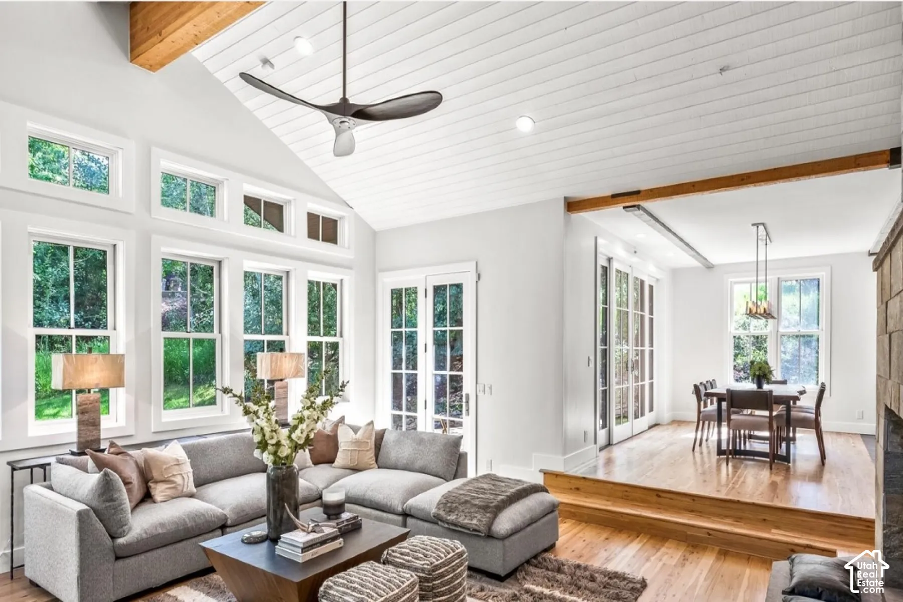 Vaulted wood-paneled ceiling, exposed wood beam accents, expansive multi-pane windows, wood-finish flooring, and a built-in stone fireplace