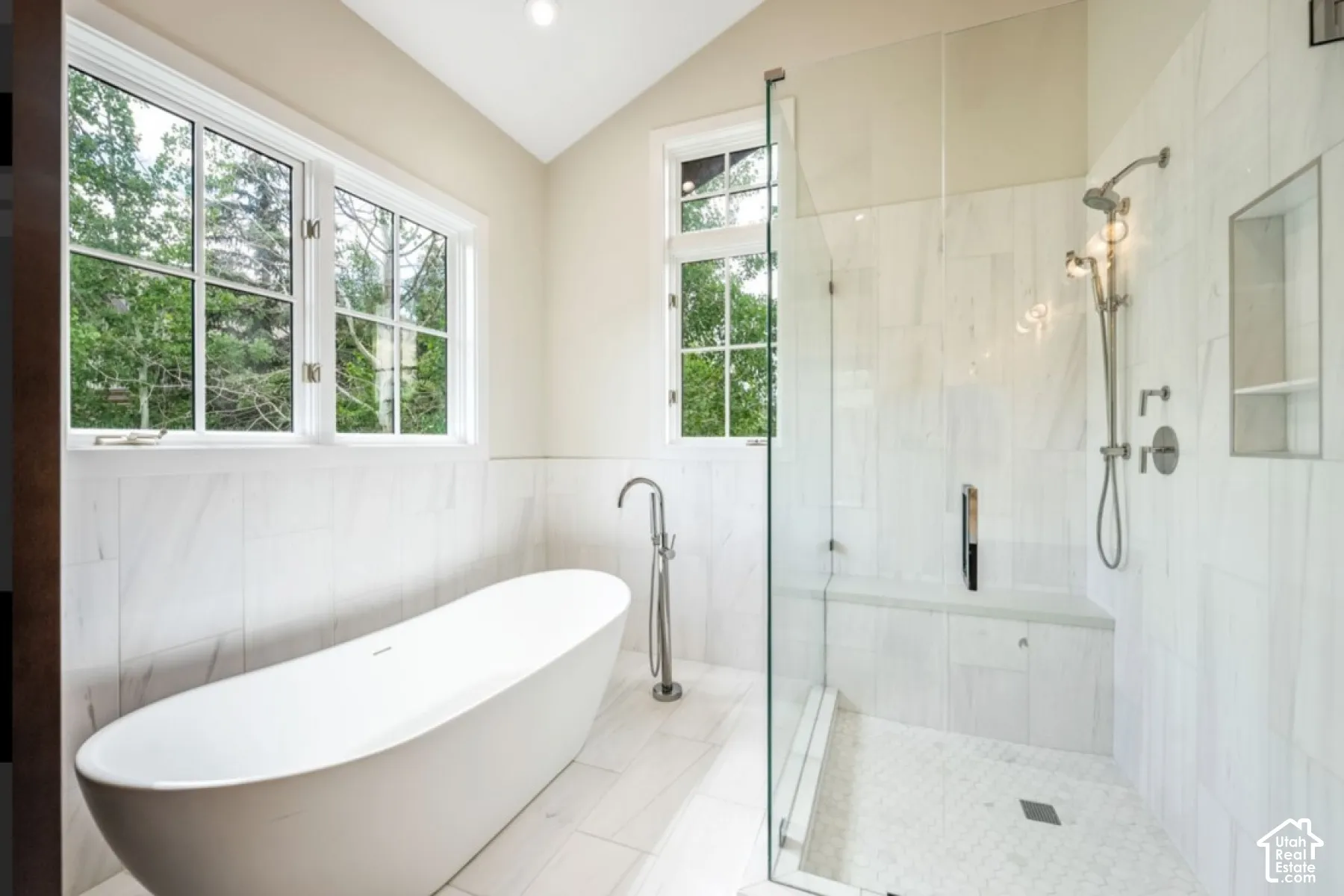 Freestanding soaking tub with a floor-mounted faucet, walk-in shower with a glass enclosure, integrated shower bench, and recessed wall niche