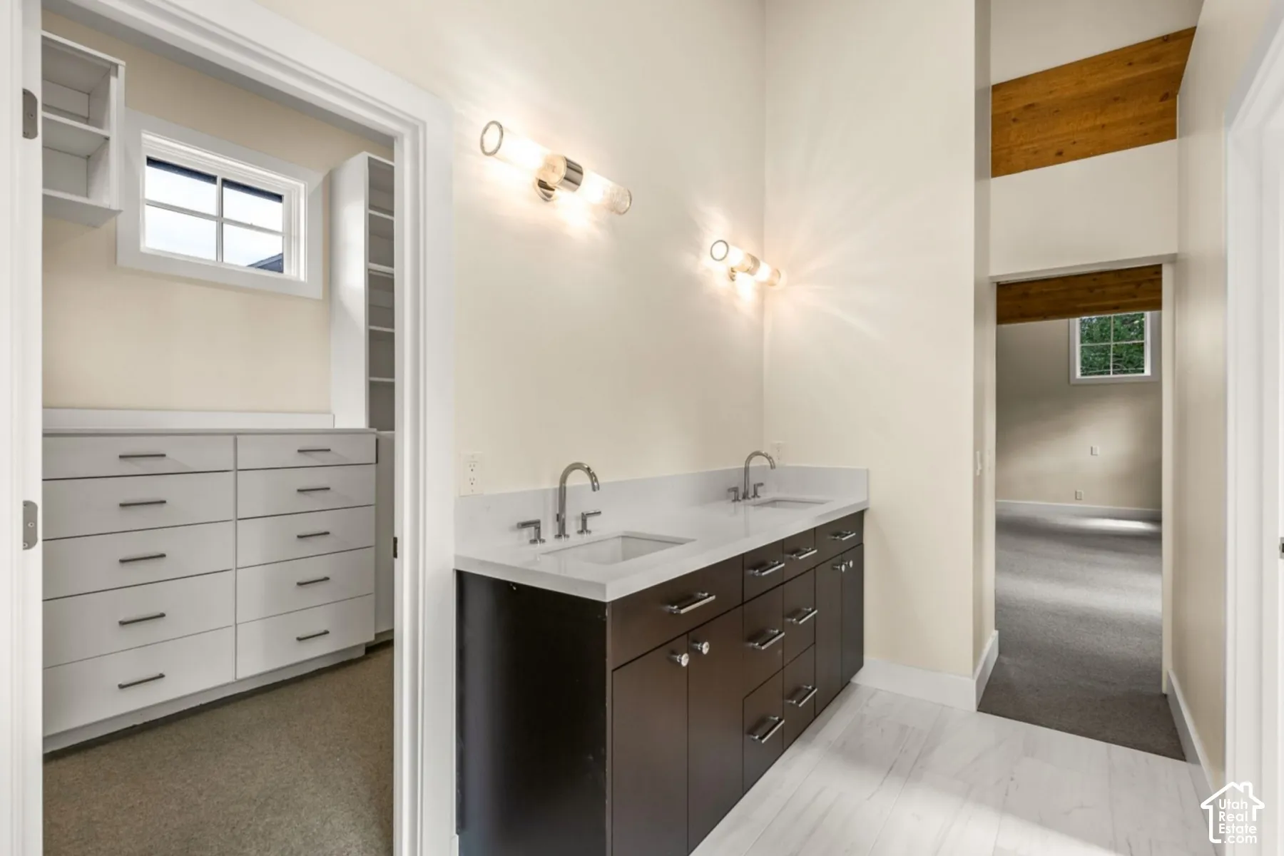 Double vanity with white countertop and integrated sinks, wood-finish cabinetry, and chrome fixtures