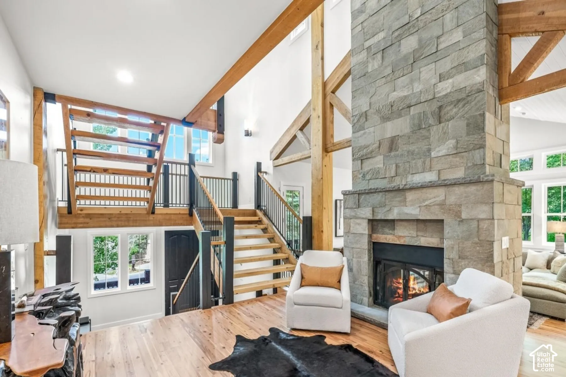 Two-story stone-clad fireplace, exposed wood beams, wood-finish flooring, staircase with wood treads and metal balusters, and a second-story landing with wood and metal railing