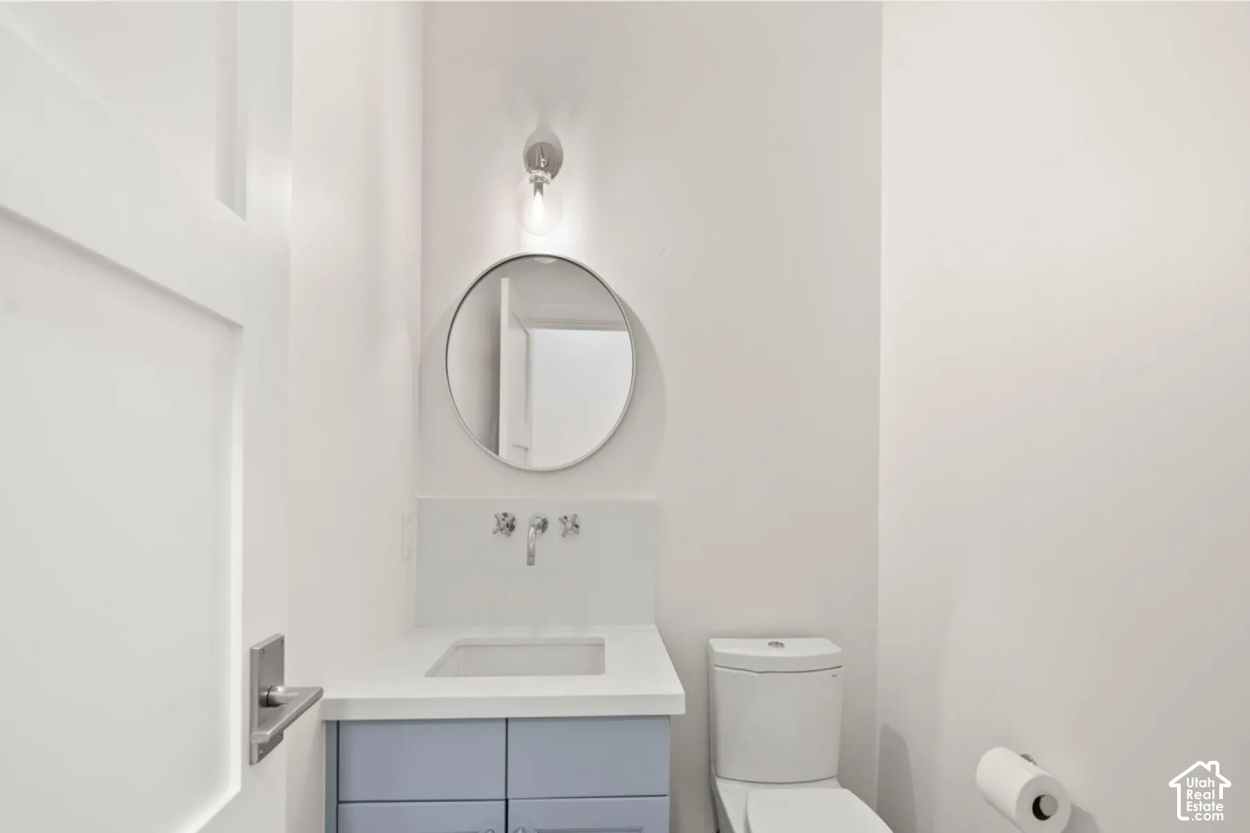 Vanity with a light blue cabinet and white countertop, a circular mirror, and a wall-mounted faucet