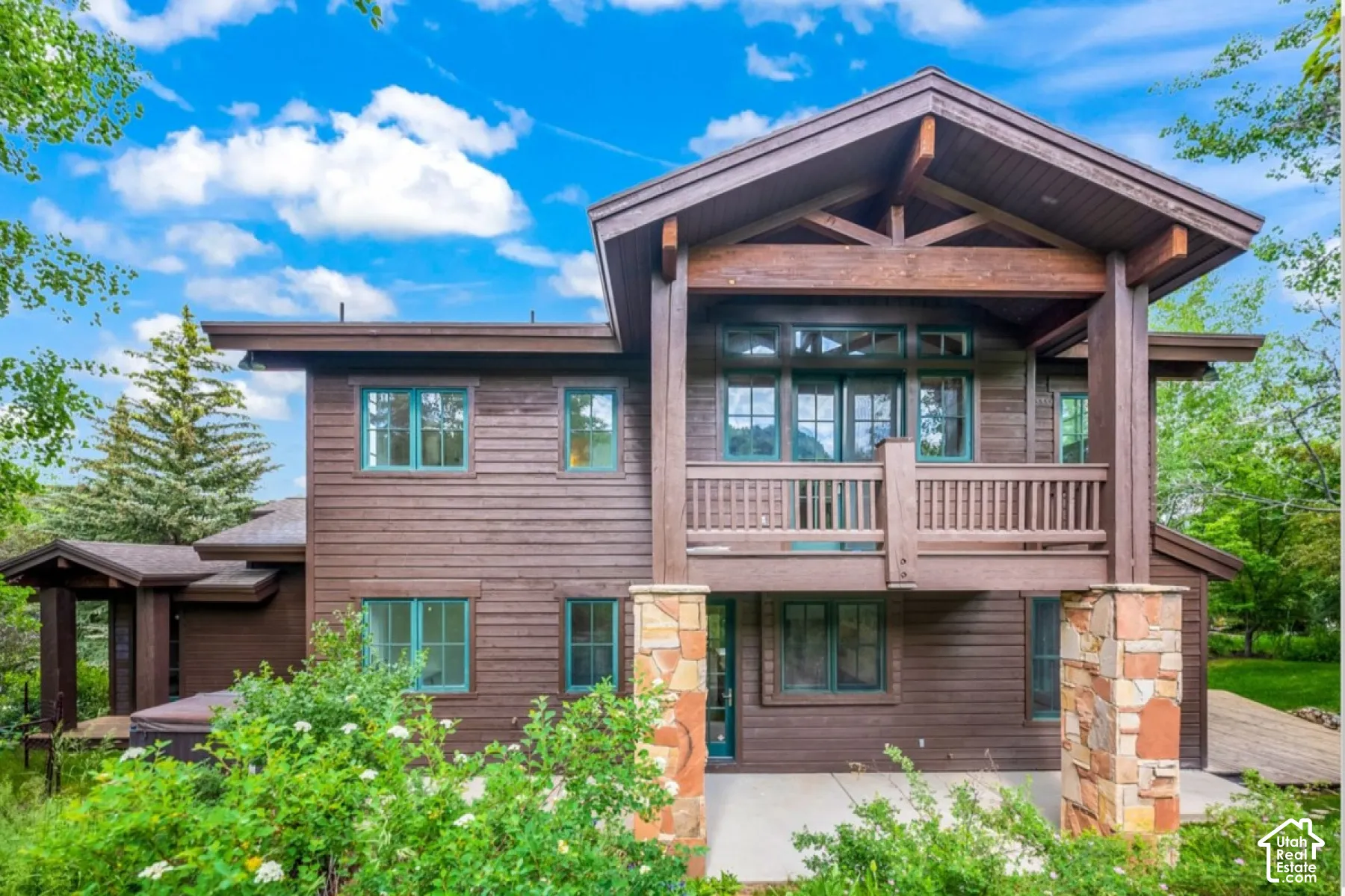 Wood-clad exterior with exposed timber framing, stone-clad pillars, multi-level balconies, and green-framed windows