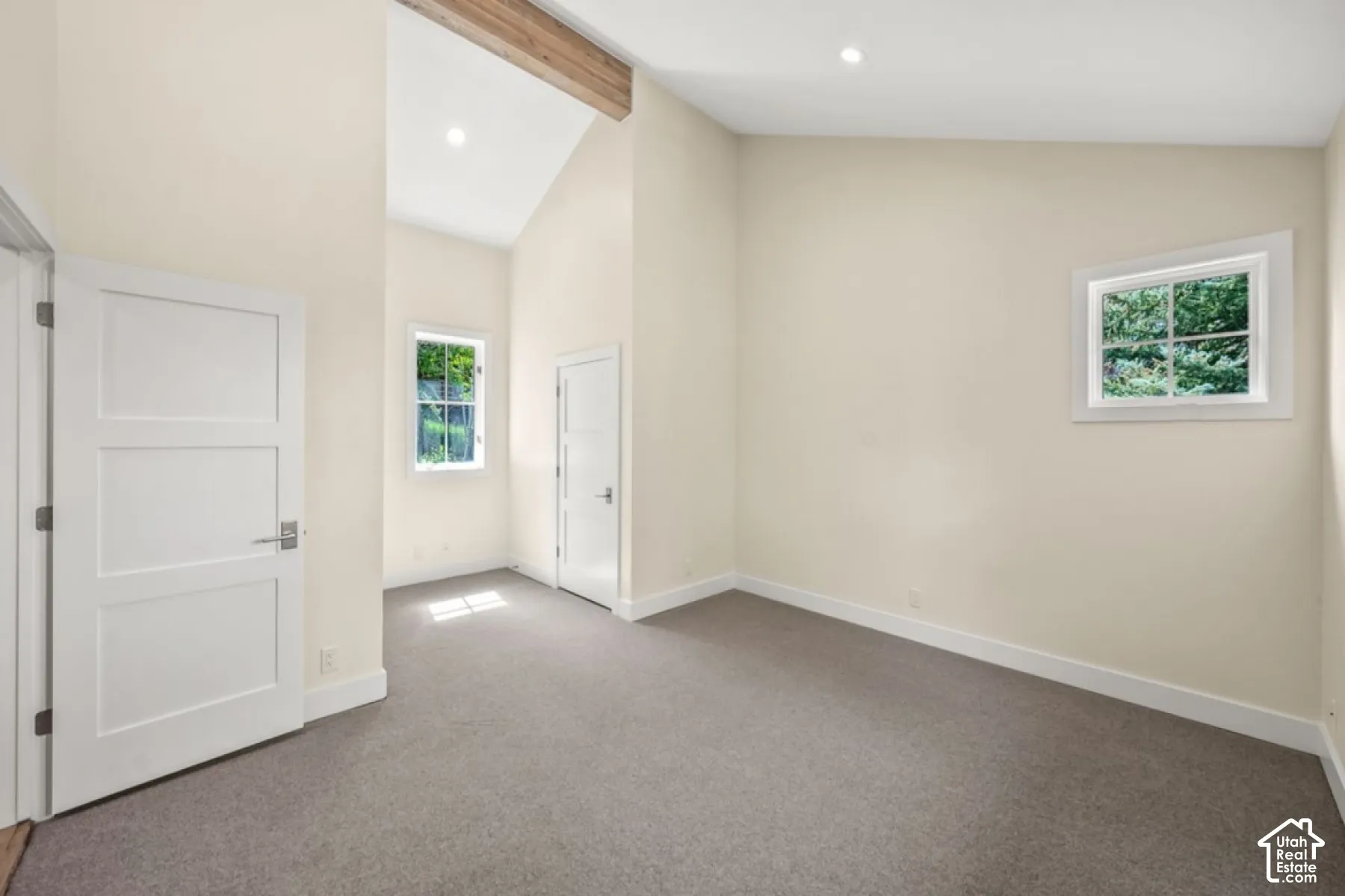 Vaulted ceiling with exposed wood beam, recessed lighting, and dual windows