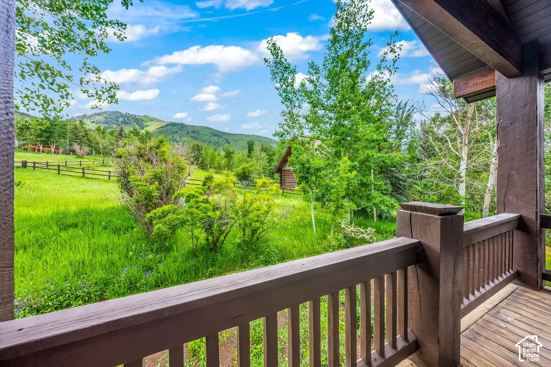 Wood-finish decking with a substantial railing, providing an expansive natural landscape with distant hills, lush trees, and open green space