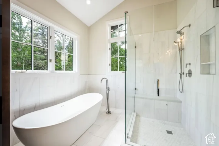 Freestanding soaking tub with a floor-mounted faucet, walk-in shower with a glass enclosure, integrated shower bench, and recessed wall niche