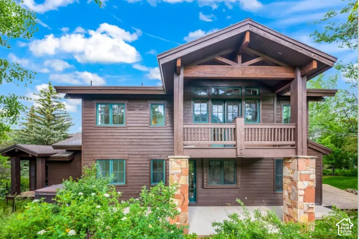 Wood-clad exterior with exposed timber framing, stone-clad pillars, multi-level balconies, and green-framed windows