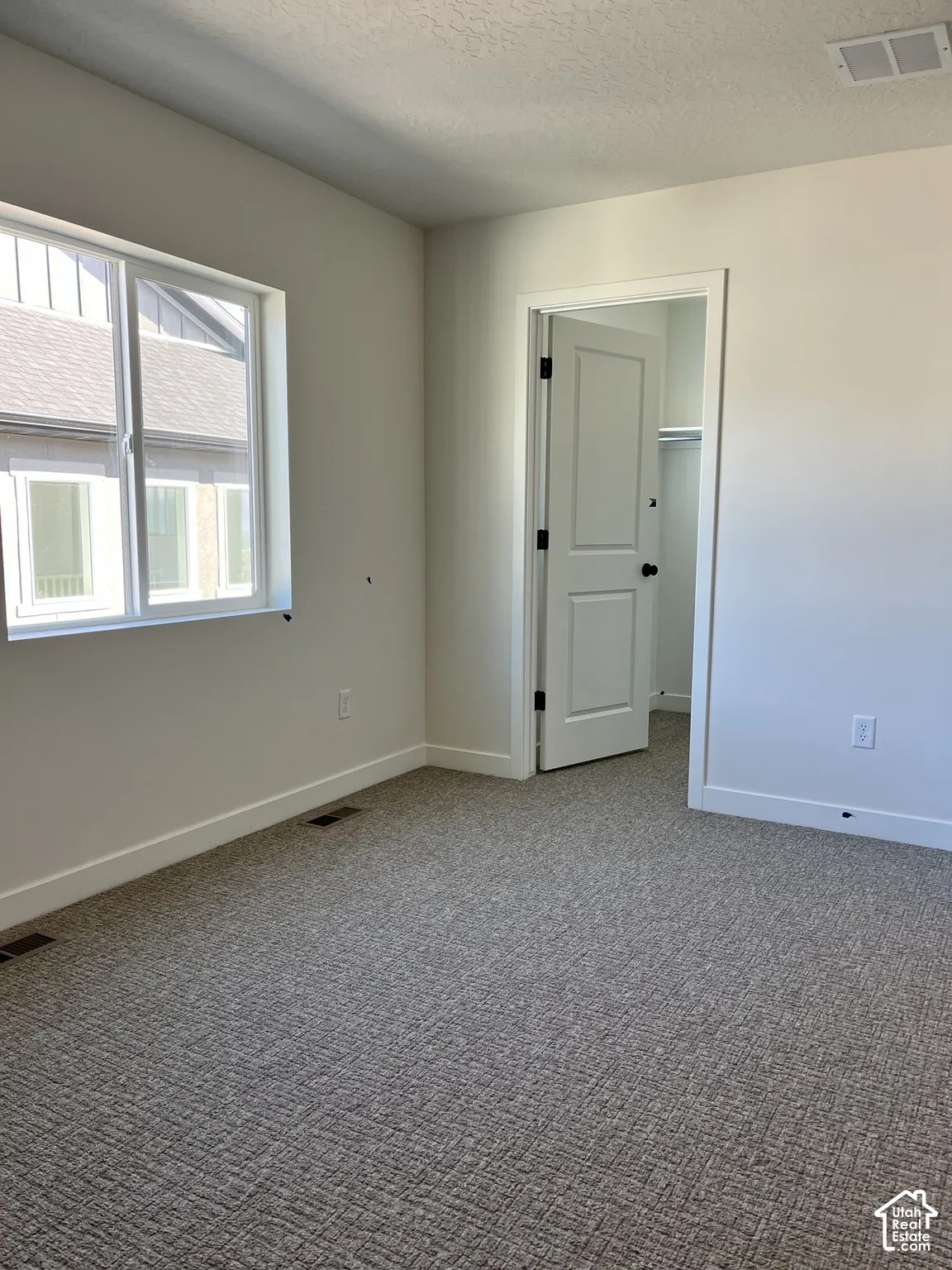 Wall-to-wall textured carpeting, a white interior door with black hardware, and a double-pane window