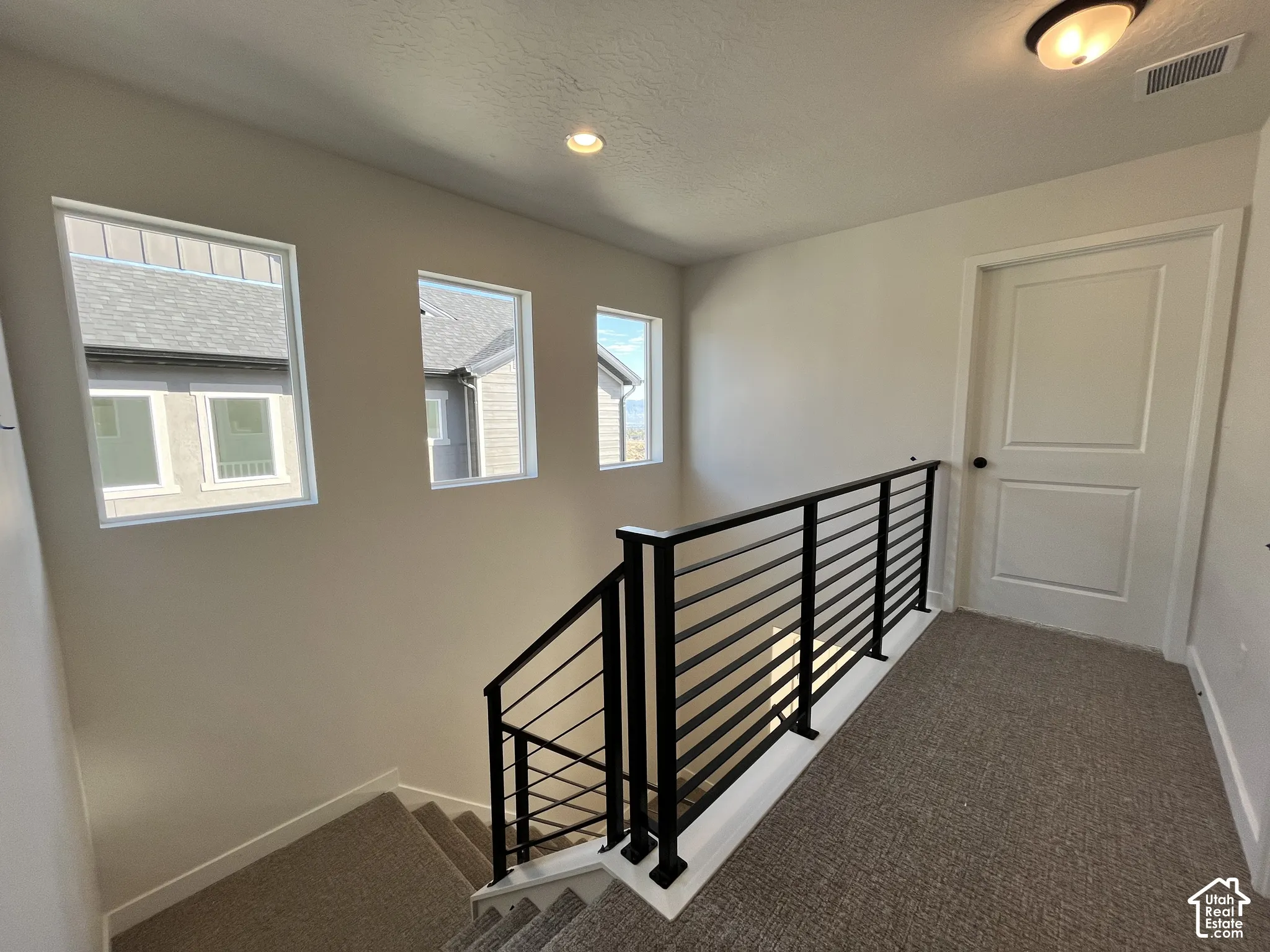 Modern black horizontal rod railing, three rectangular windows, recessed ceiling lighting, and neutral tone carpeting
