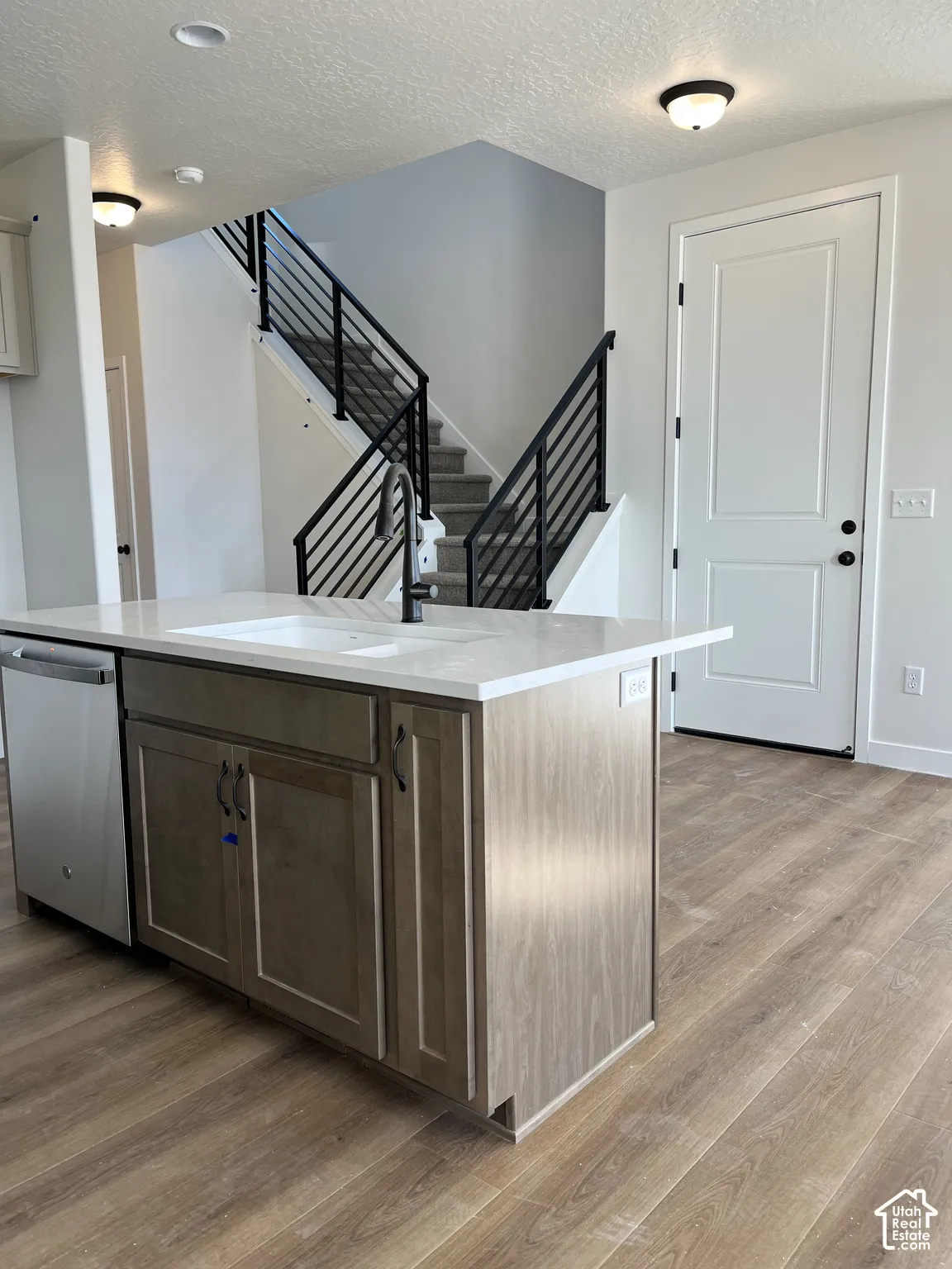 Kitchen island with wood-finish cabinetry, integrated sink, and stainless steel dishwasher