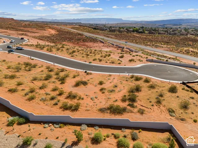 Paved cul-de-sac, undeveloped desert terrain, partial retaining wall, distant mountains, and established roadway