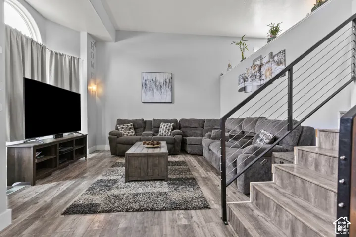 Living area featuring wood-finish flooring, a wall-mounted sconce, and a staircase with a cable railing system