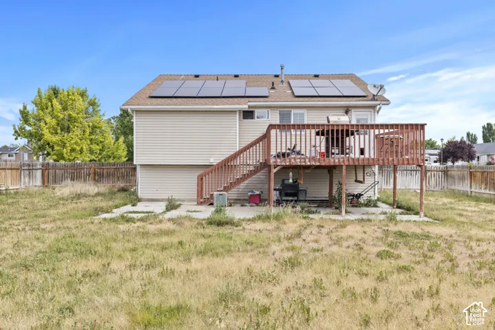 Rear exterior with solar panels, a raised wooden deck with railings, and neutral-toned siding