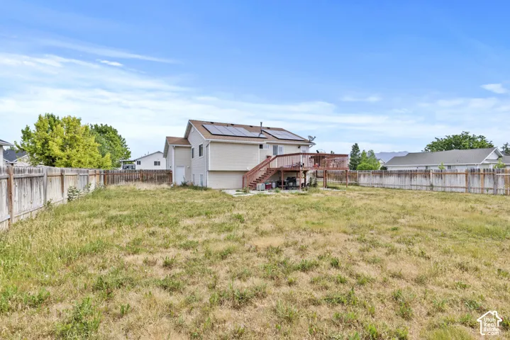 Expansive backyard featuring a full perimeter fence, multi-level wood deck, and solar panels on the roof