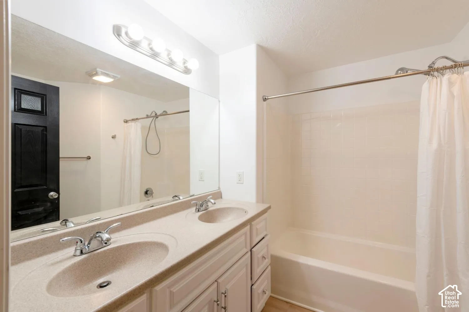 Double vanity with integrated sinks, chrome fixtures, built-in cabinetry, full-width mirror, and a tub/shower combination