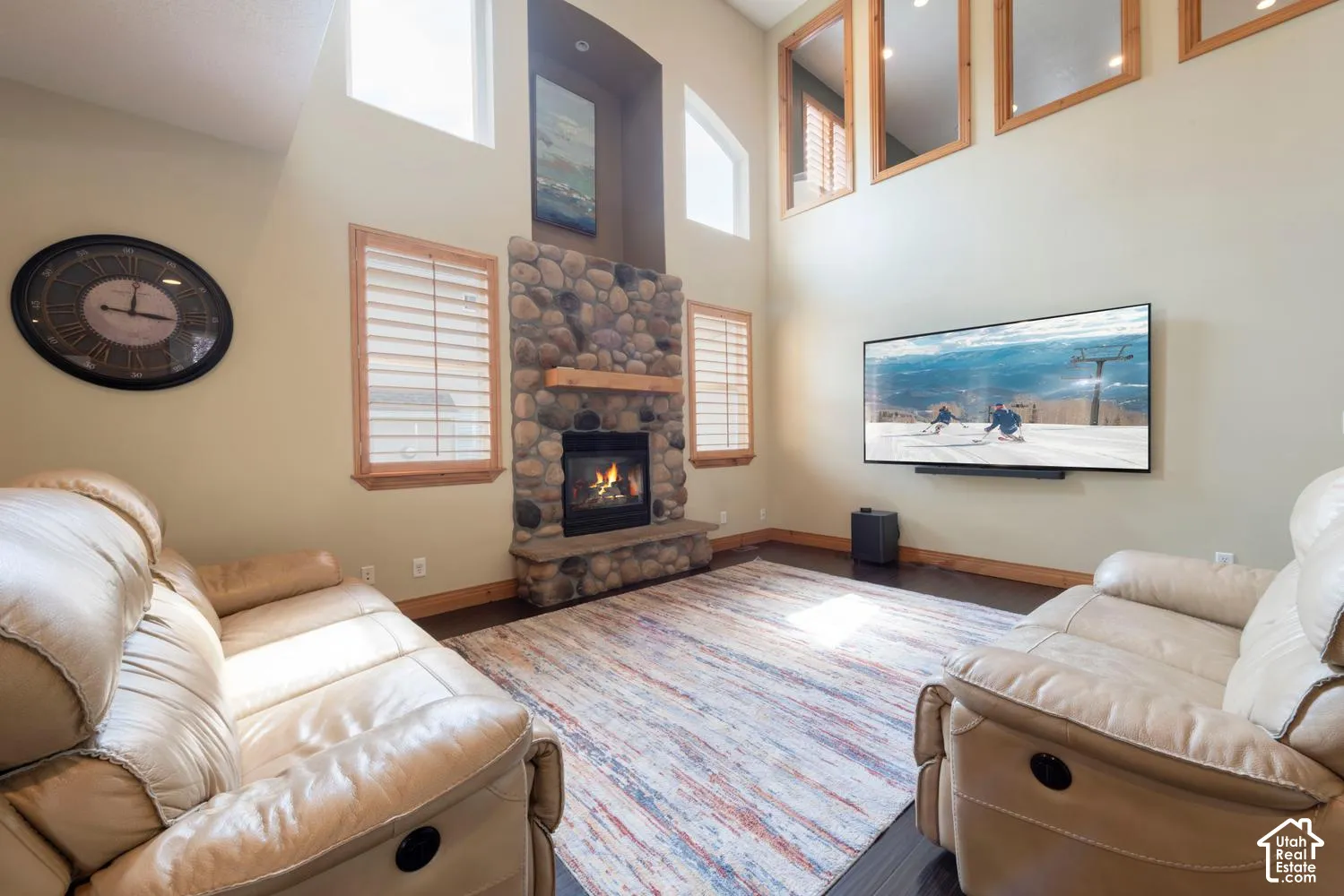 Vaulted ceilings, a stone-clad fireplace with a wood mantel, wood-finish flooring, and high windows providing natural light