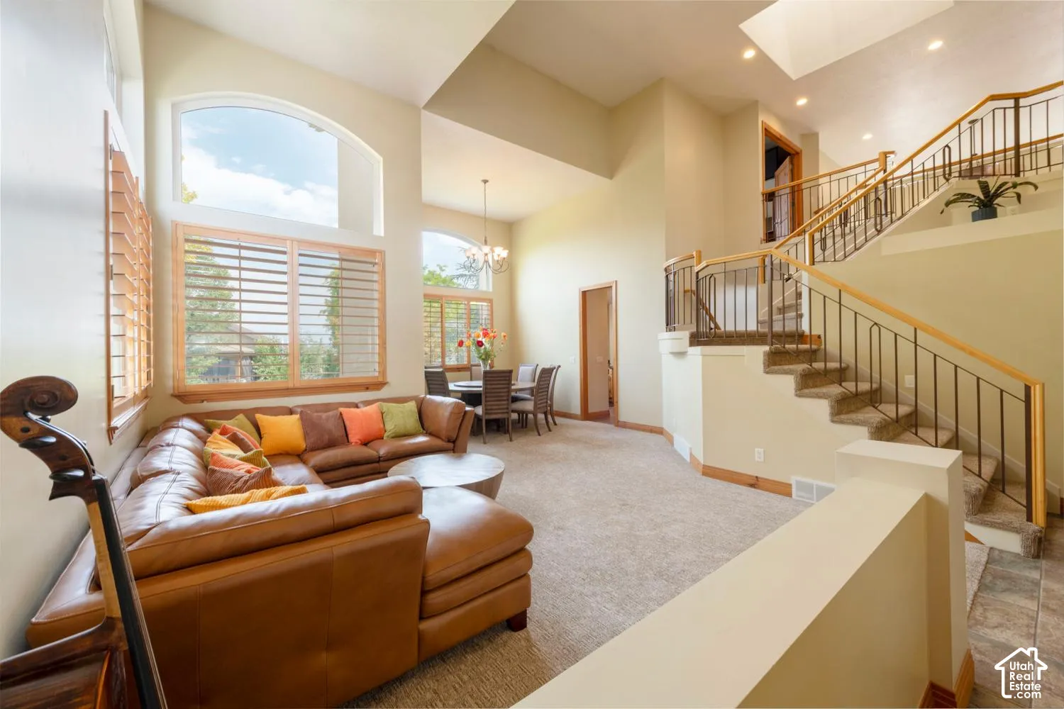 Two-story vaulted ceilings, arched windows with plantation shutters, wrought iron stair railing with wood handrail, recessed lighting, and carpeted flooring
