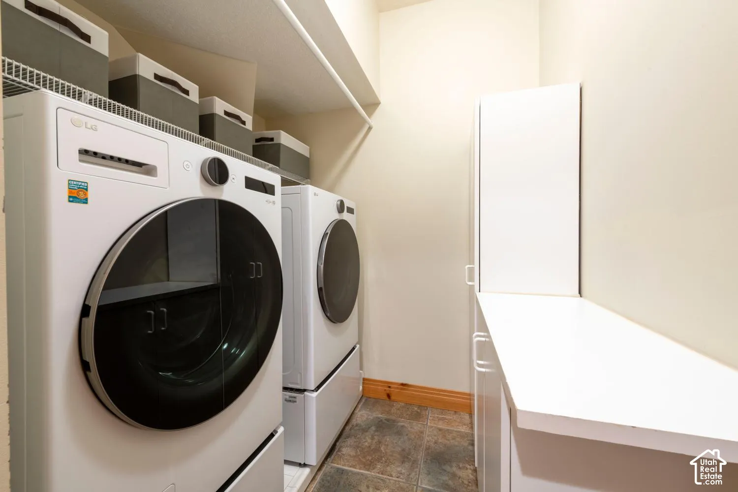 Laundry area featuring a shelf, white cabinetry, and stone tile flooring