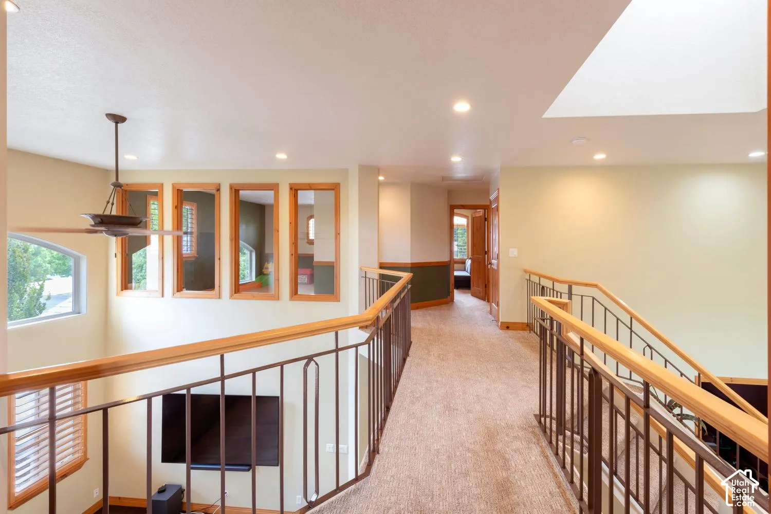 Carpeted hallway with wood and wrought iron railings, recessed lighting, and a skylight