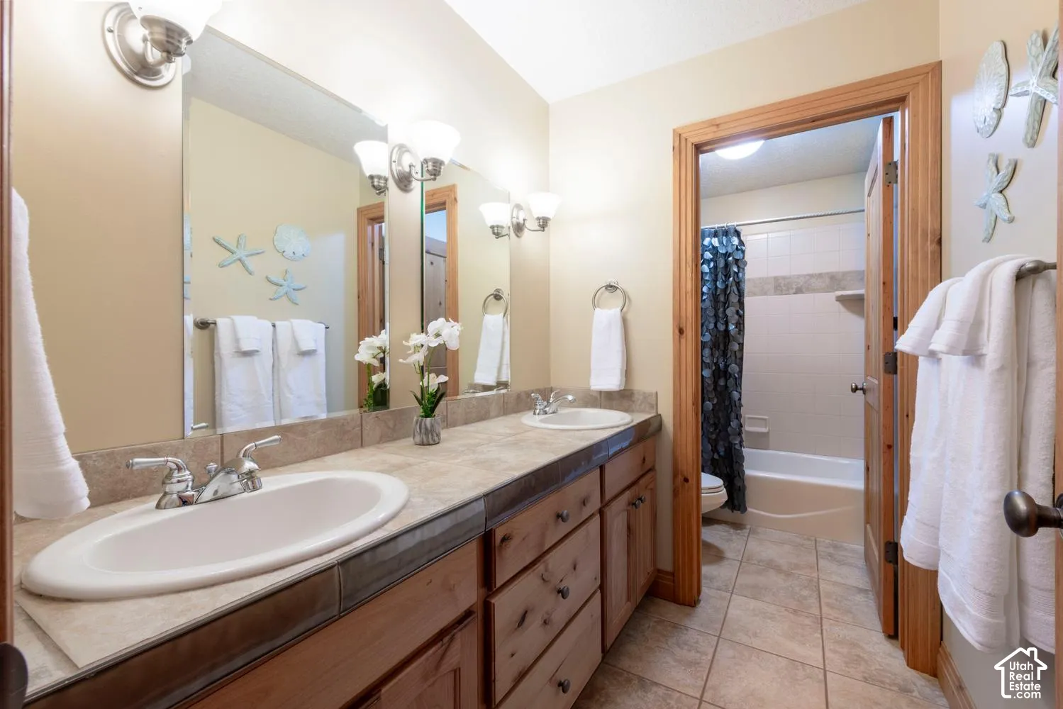 Double vanity with individual sinks, wood-finish cabinetry, tile countertop, and tile flooring