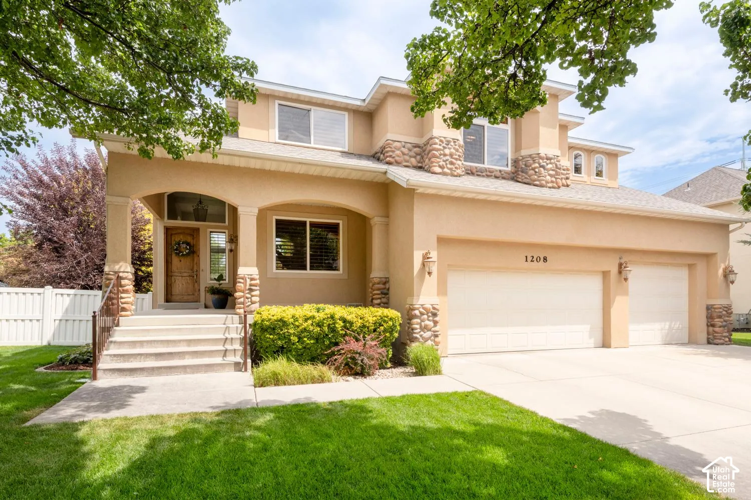 Stucco exterior with stone accents, covered entry porch, double garage with individual doors, established front landscaping, and concrete driveway