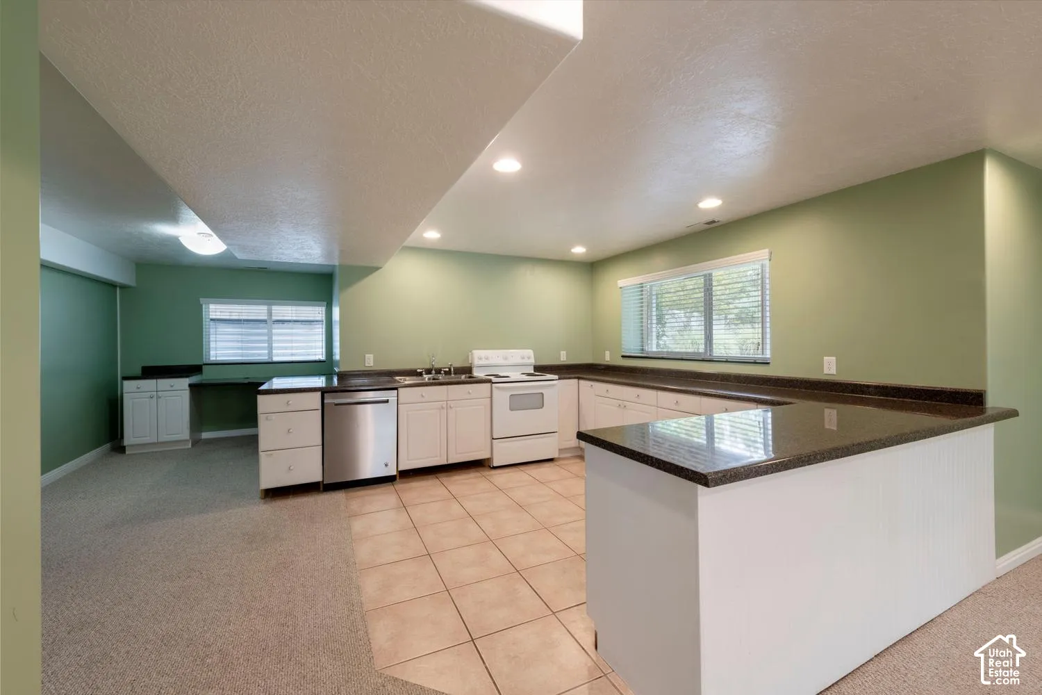 U-shaped kitchen featuring white cabinetry, dark countertops, a stainless steel dishwasher, and tiled flooring