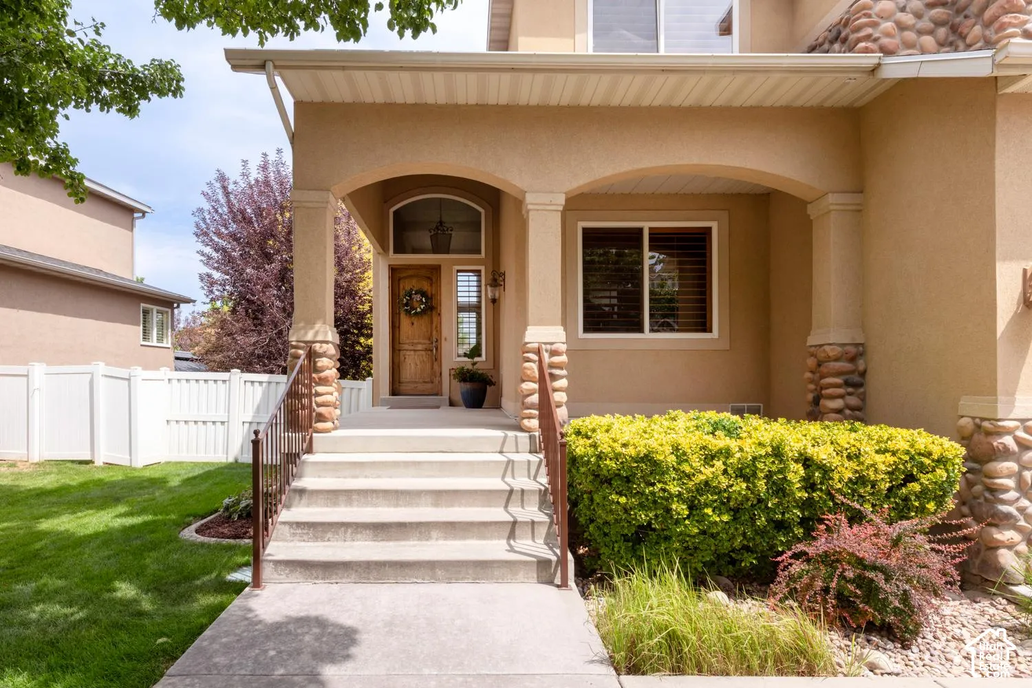 Stucco exterior with stone accents, covered entry porch, wood-finish front door with arched transom, and concrete steps with metal railings