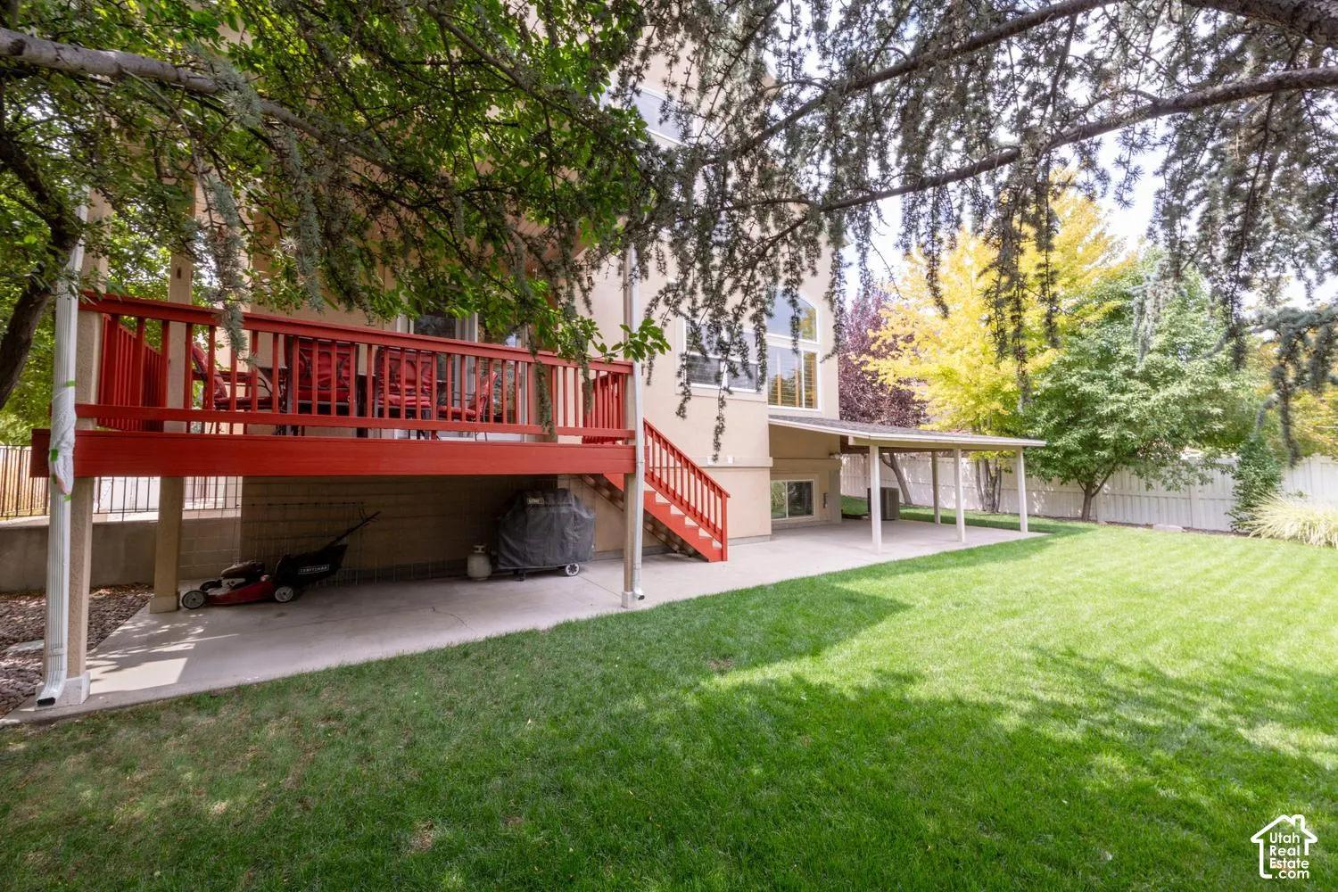 Expansive lawn with a red wooden deck, a covered patio, and mature trees