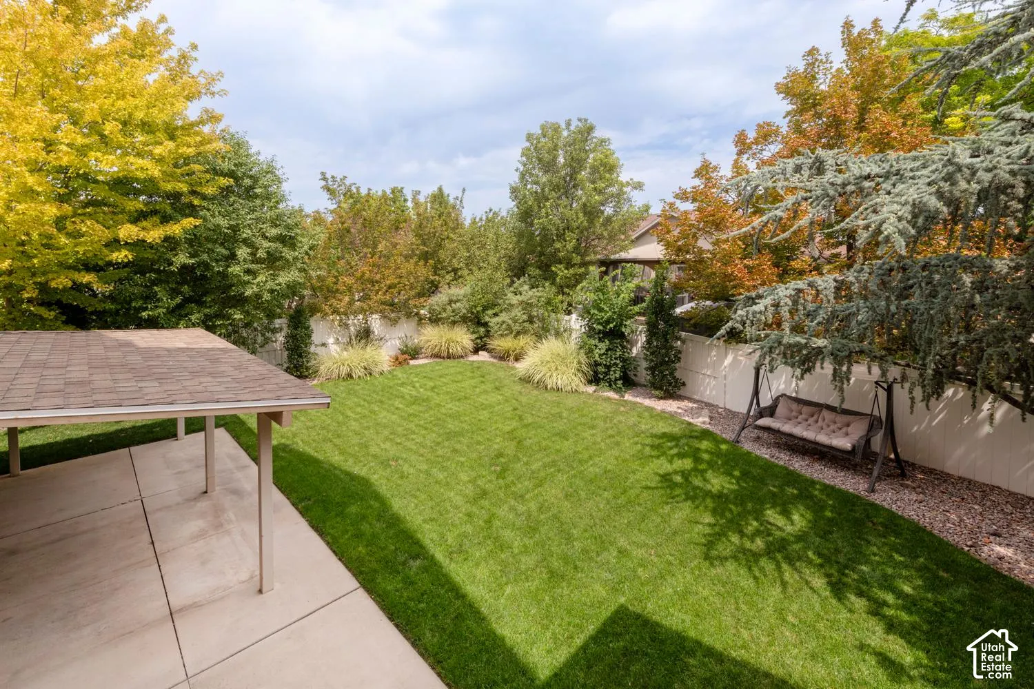Expansive backyard featuring a manicured lawn, established perimeter landscaping, and a covered concrete patio