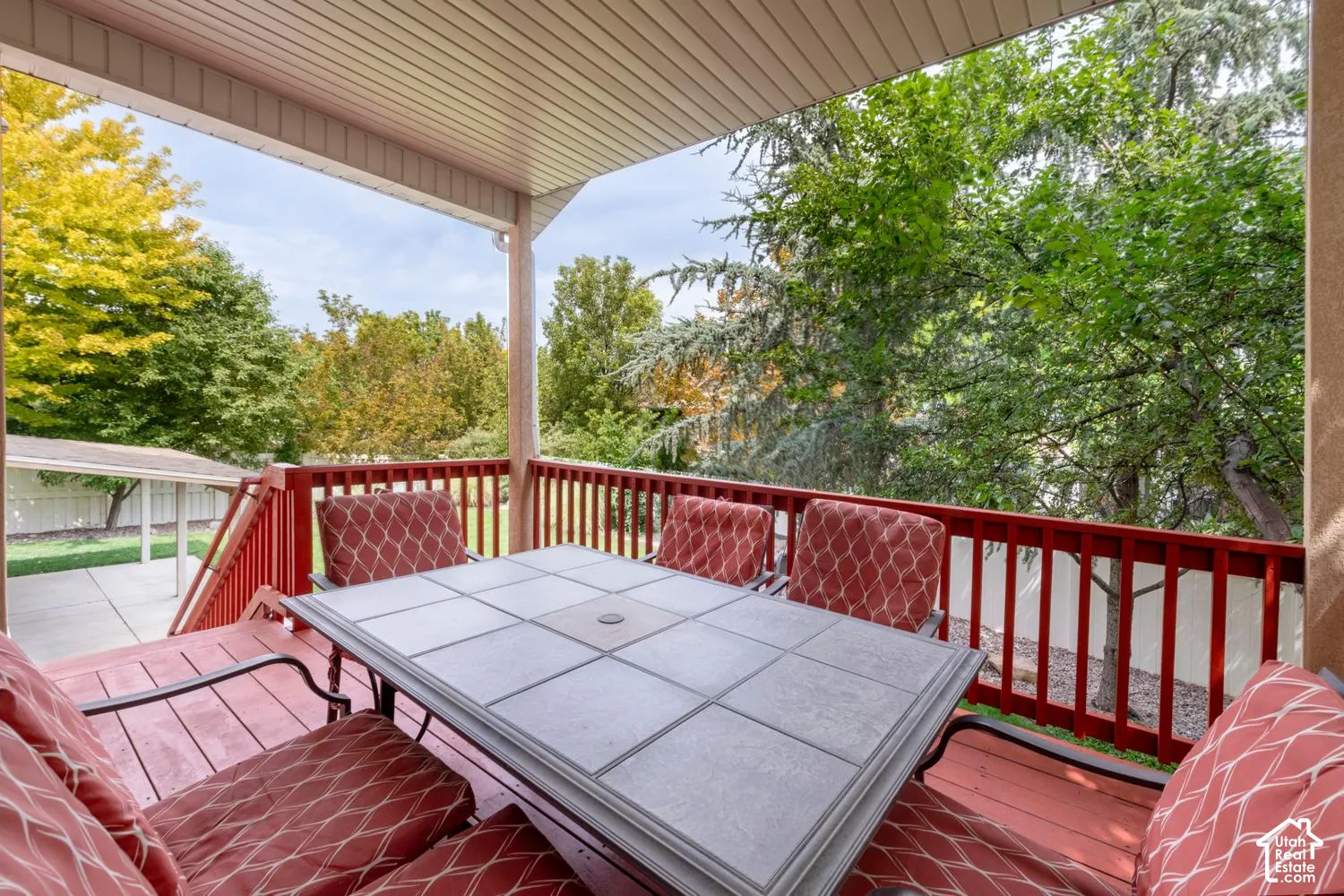 Covered outdoor deck with red-stained wood railing and flooring, featuring a tiled tabletop