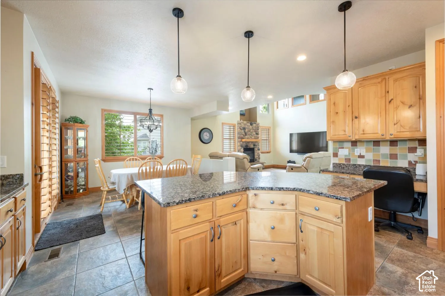 Kitchen featuring wood cabinetry, stone countertops, tile flooring, pendant lighting, and a built-in desk area