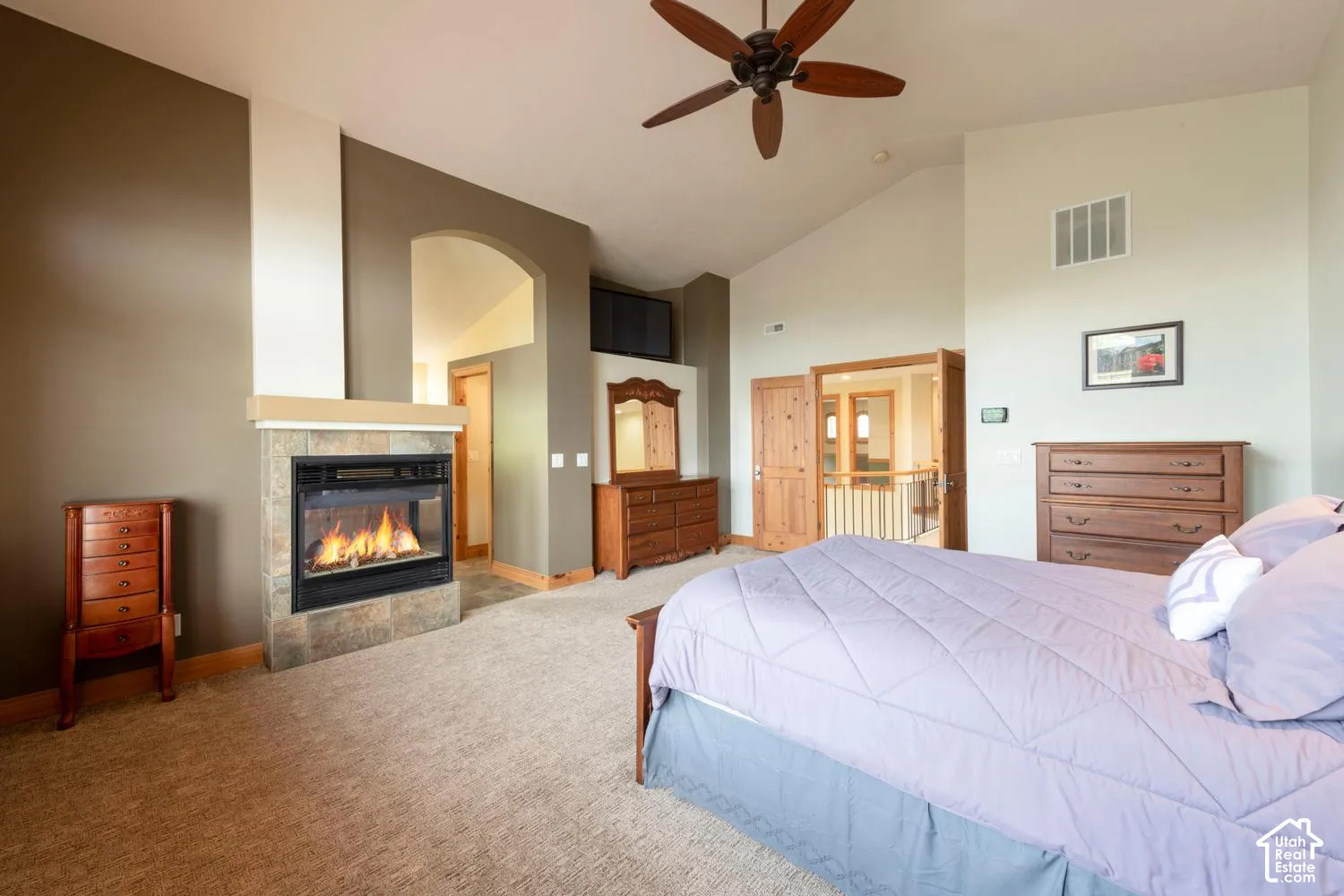 Vaulted ceiling, ceiling fan, carpeted flooring, built-in fireplace with stone surround, and wood-finish doors