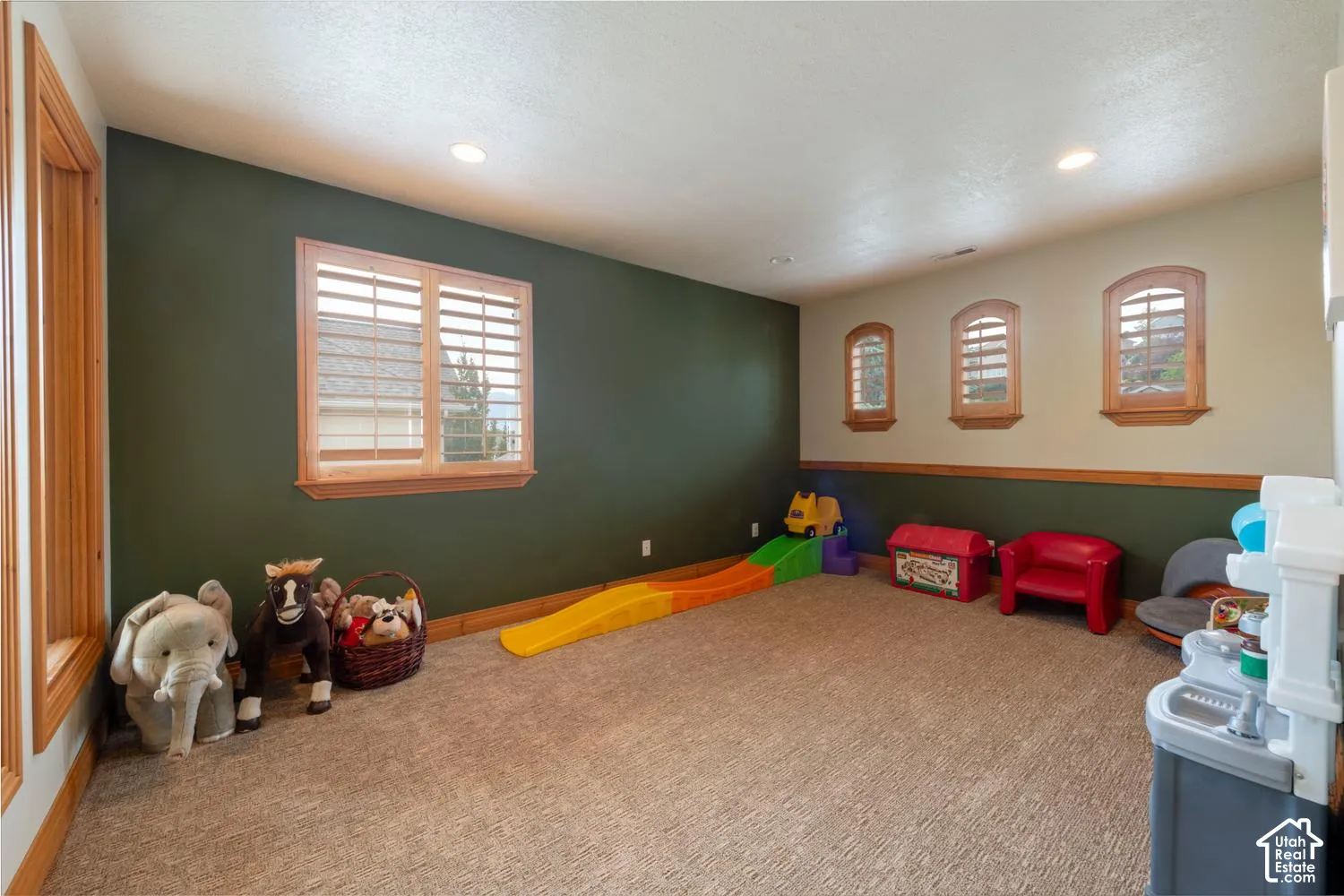 Recessed lighting illuminates a spacious room featuring a primary window with plantation shutters and three arched windows with wood trim