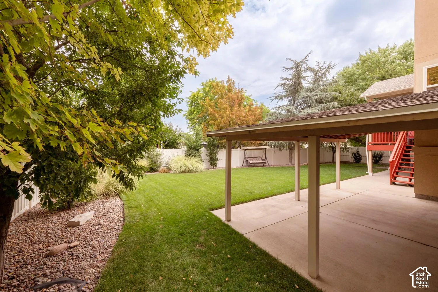 Expansive backyard featuring a covered patio, manicured lawn, and mature trees