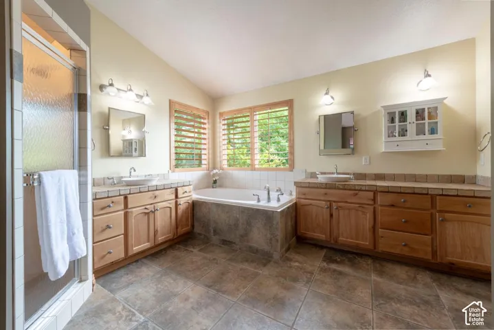 Dual wood-finish vanities with vessel sinks, a built-in soaking tub, tile flooring, and a glass-enclosed shower