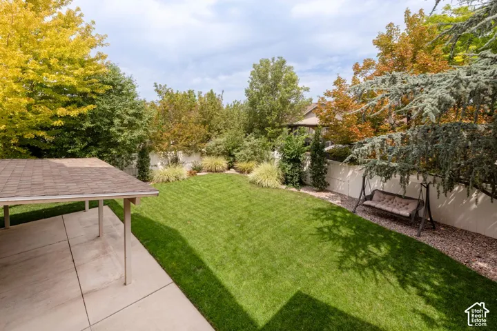 Expansive backyard featuring a manicured lawn, established perimeter landscaping, and a covered concrete patio