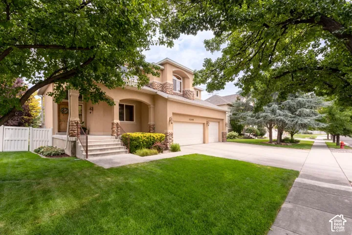 Stucco exterior with stone accents, covered front entry, two-car garage, concrete driveway, and front lawn