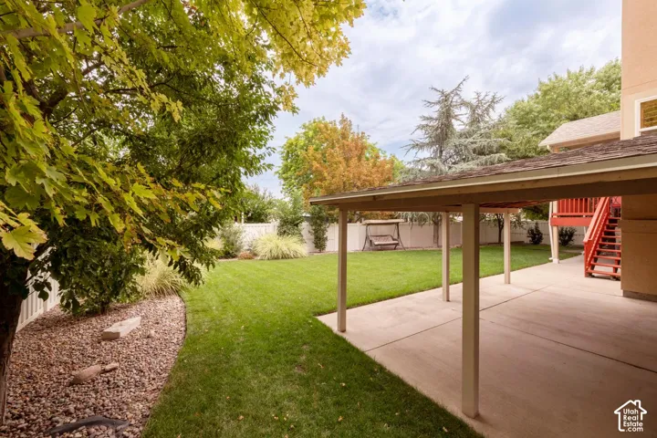 Expansive backyard featuring a covered patio, manicured lawn, and mature trees
