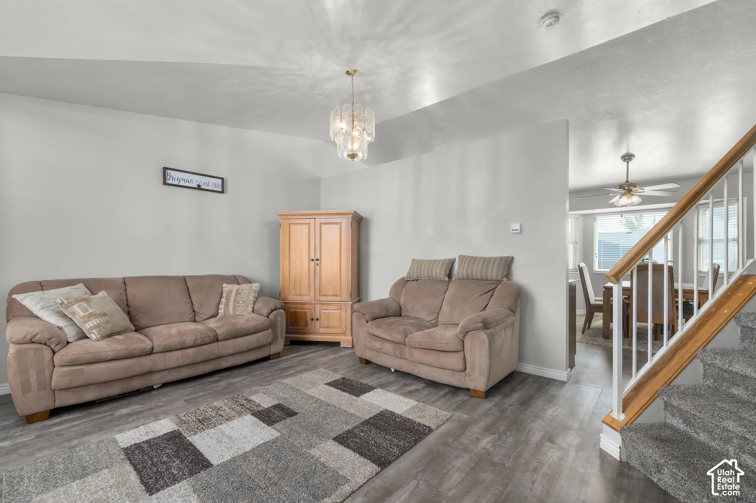 Wood-finish flooring, staircase with white spindles and wood handrail, ceiling-mounted light fixture, and neutral wall paint