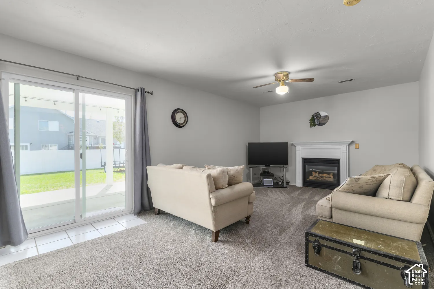 Sliding glass door, tiled flooring, carpeted living area, fireplace with white mantel, and ceiling fan