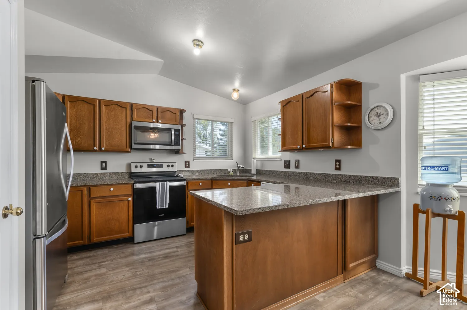 Kitchen with wood-finish flooring, wood cabinetry, stone-look countertops, and stainless steel appliances