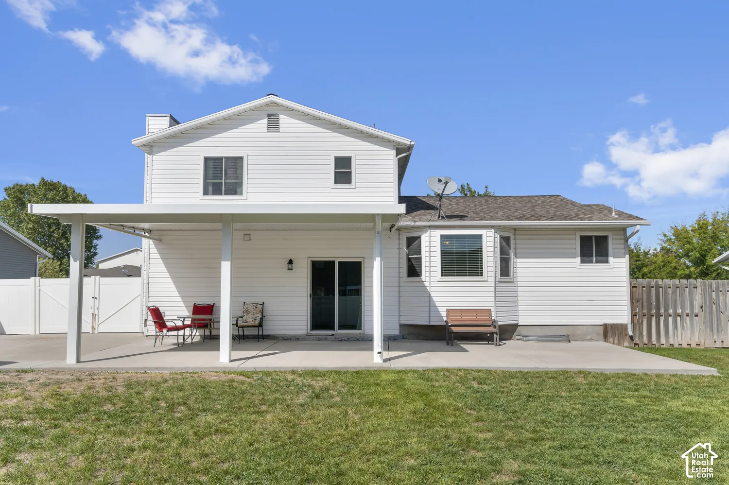 Expansive patio with a covered section, mature grass lawn, white vinyl siding, and a privacy fence
