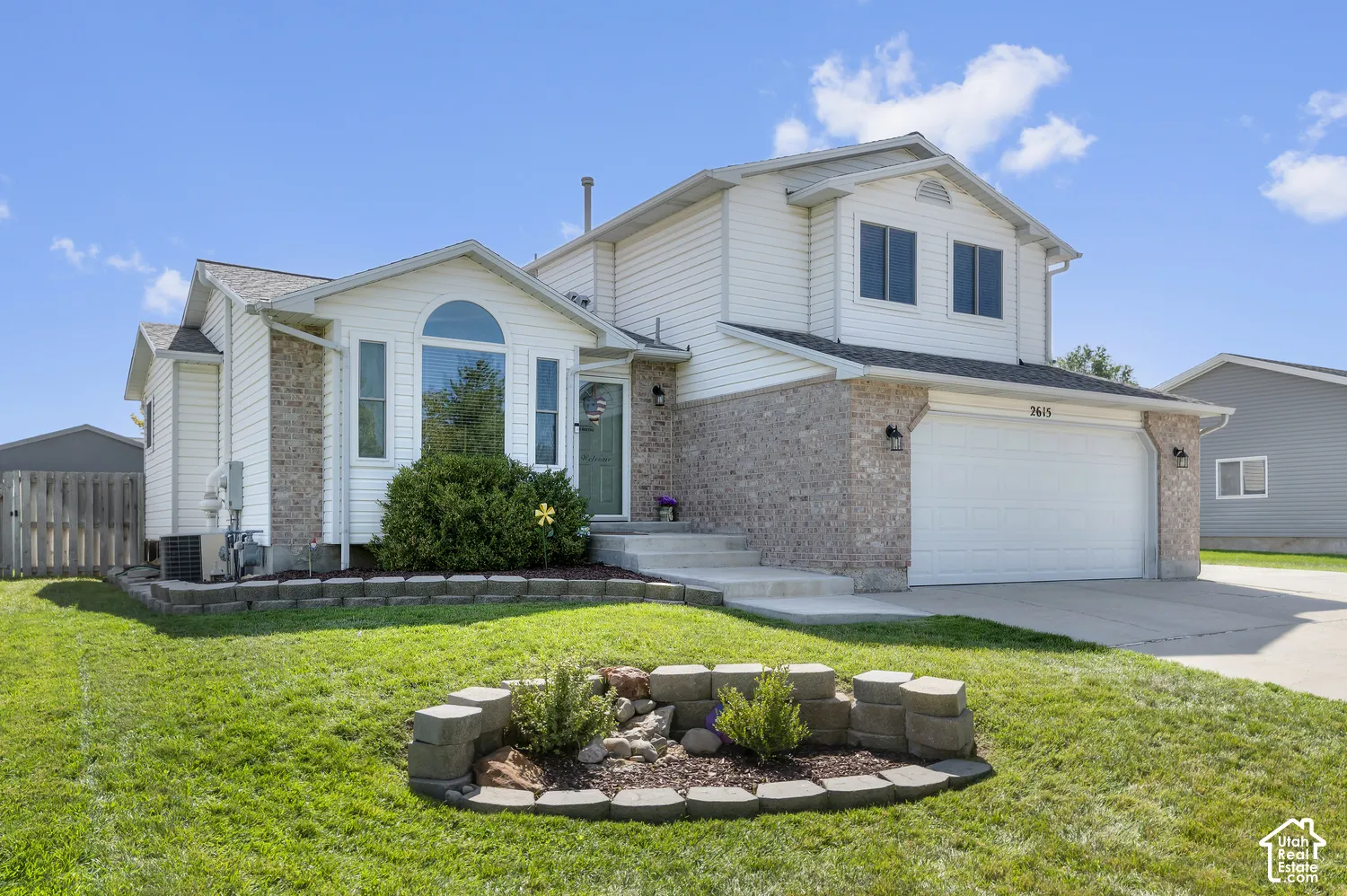 Two-story residence featuring a brick and siding exterior, an arched window, an attached two-car garage, and a landscaped front yard with a decorative stone planter