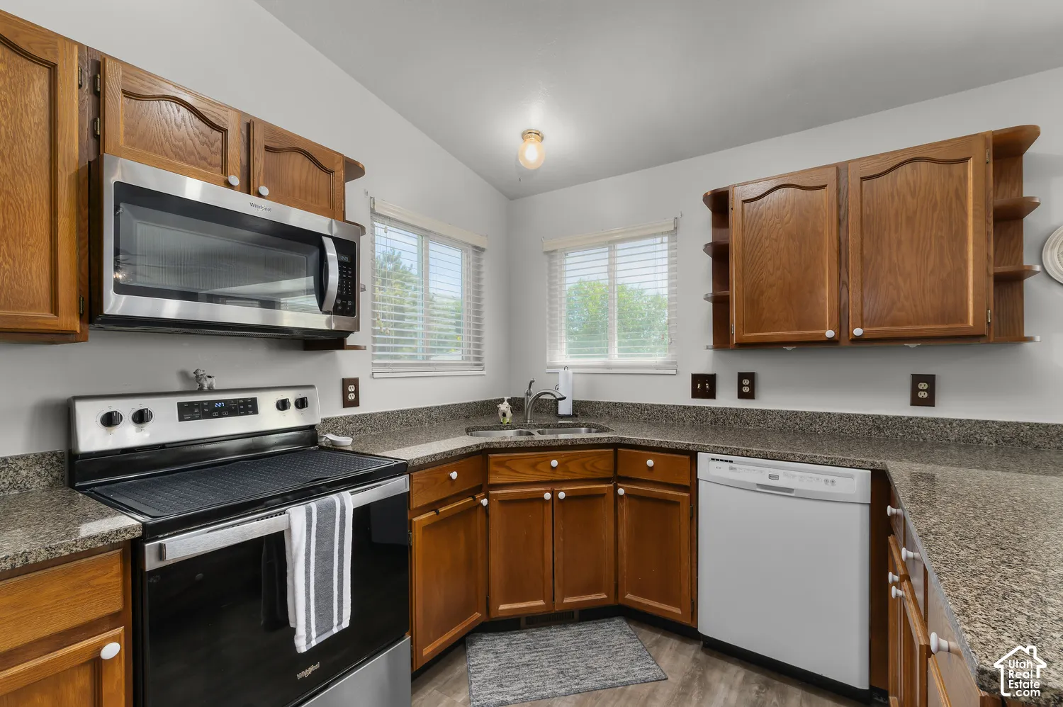Kitchen featuring wood-finish cabinetry, granite-patterned countertops, stainless steel microwave, and a stainless steel range