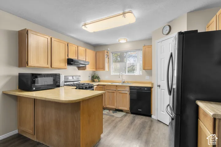 Kitchen featuring wood-finish cabinetry, black appliances, laminate countertops, and wood-look flooring
