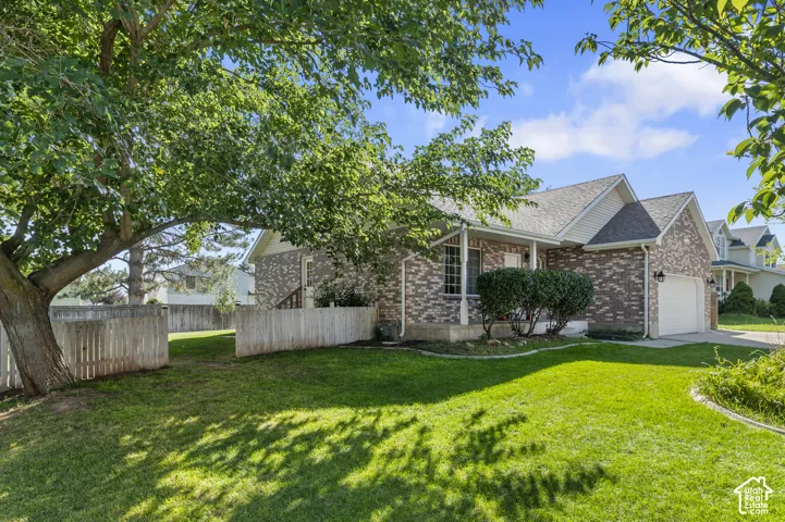 Brick exterior with gabled roofline, front porch, attached garage, manicured lawn, and mature trees