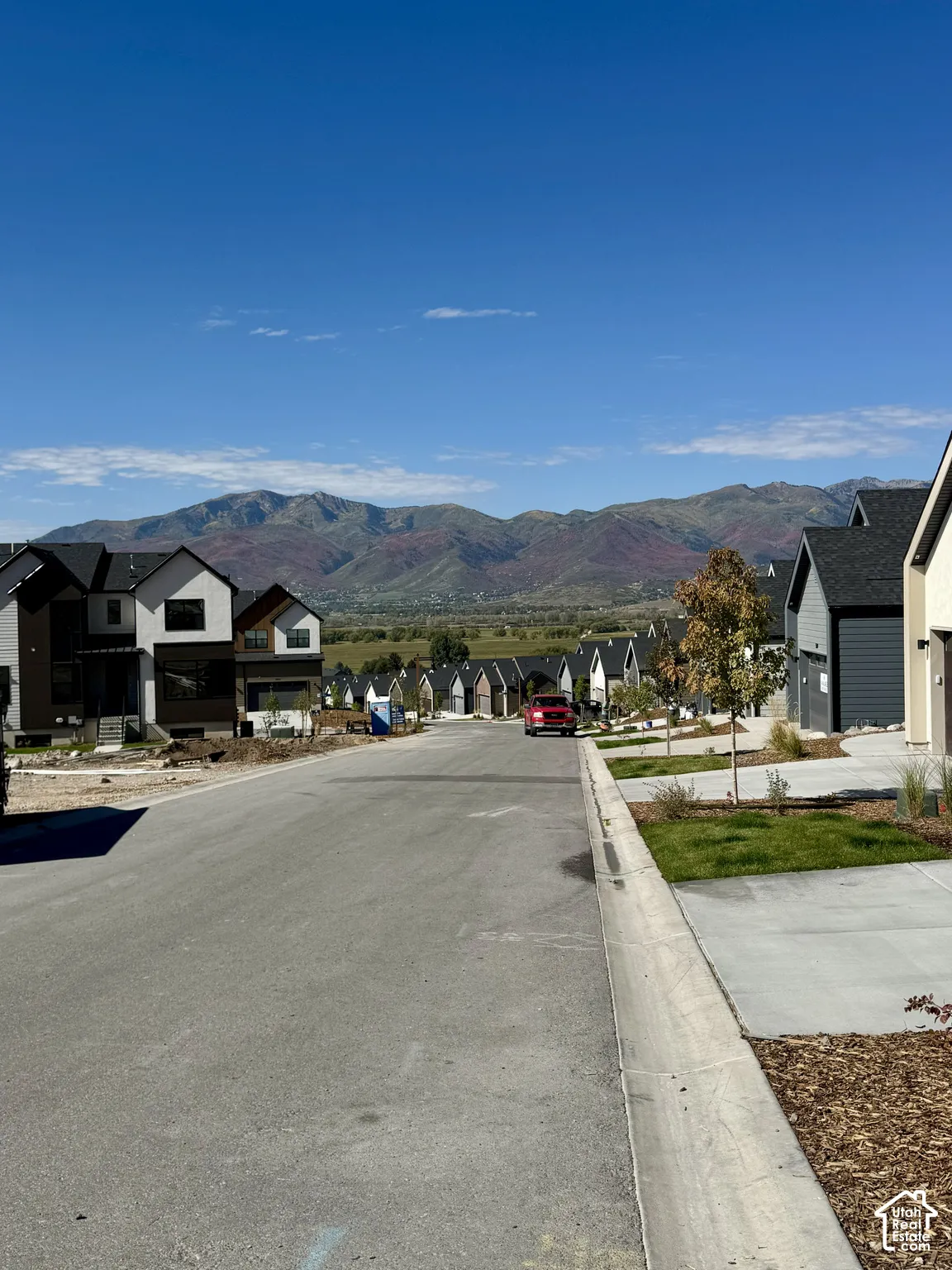 Mountain backdrop, newly constructed neighborhood with modern architecture, paved street, concrete sidewalks, and landscaped front yards