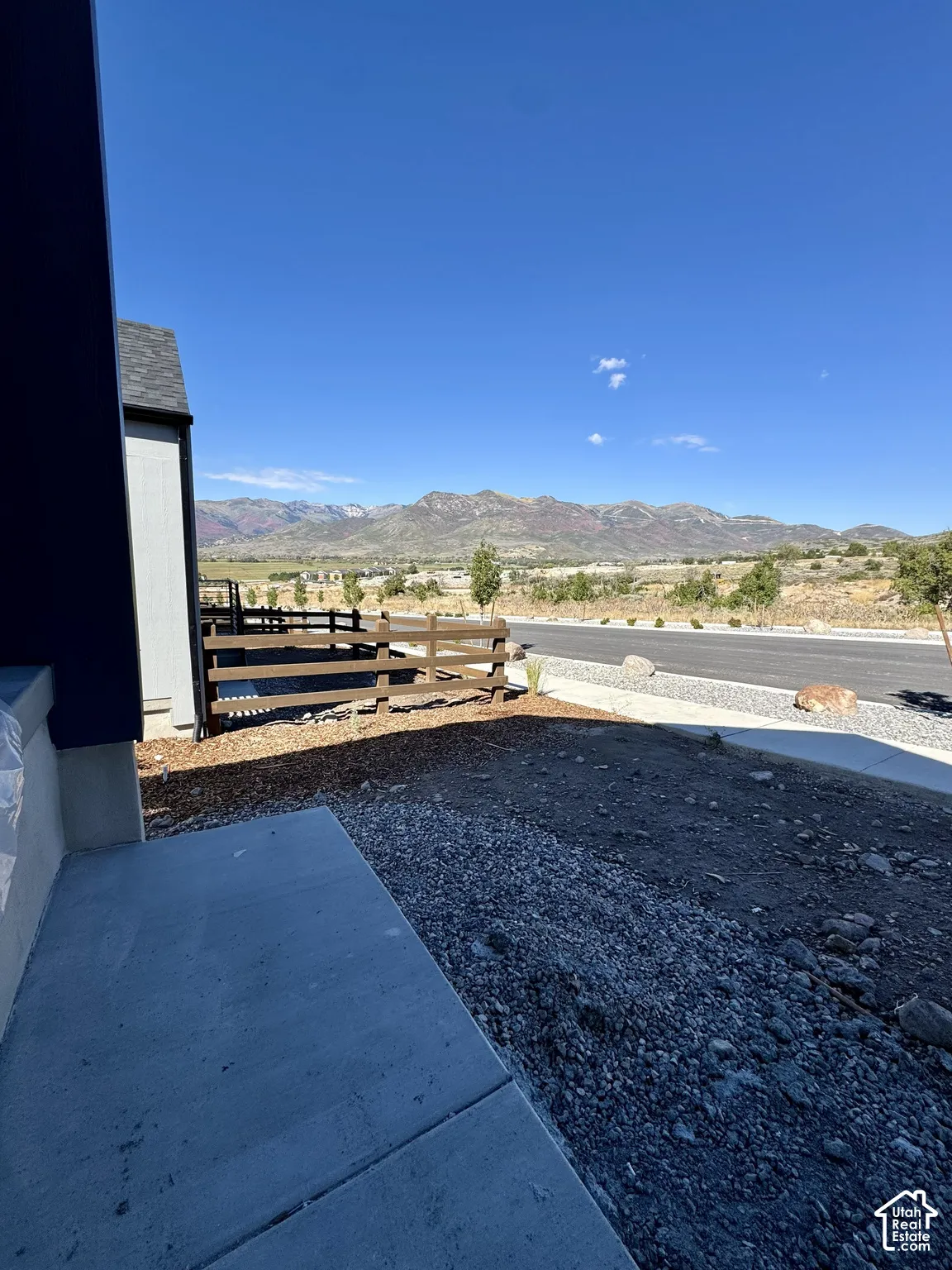 Paved concrete walkway with a partially completed exterior, featuring a wood fence, and a backdrop of distant mountains